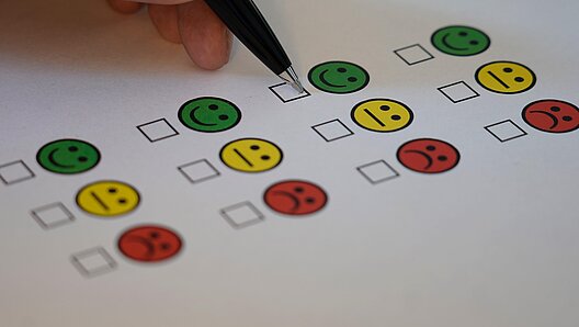 Umfrage Das Bild zeigt einen Zettel mit positiven, neutralen und negativen Smileys auf einem Umfragebogen sowie eine Hand mit Stift.