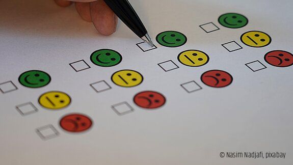 Umfrage Das Bild zeigt einen Zettel mit positiven, neutralen und negativen Smileys auf einem Umfragebogen sowie eine Hand mit Stift.